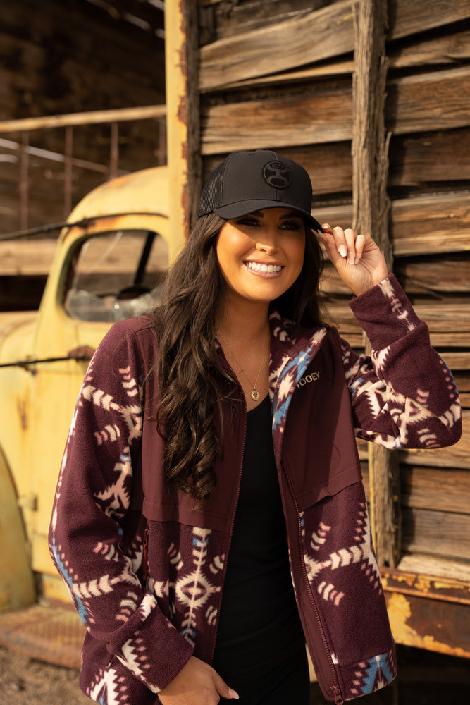 female model wearing black cap, maroon jacket, and black top