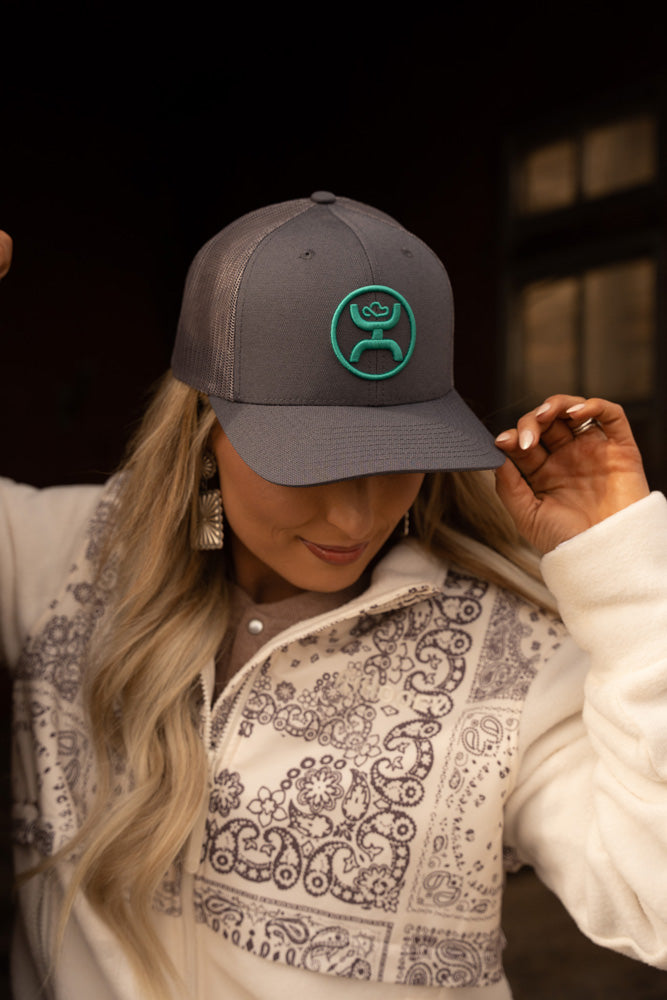 female model wearing white and black bandana pattern jacket with grey and turquoise hooey hat