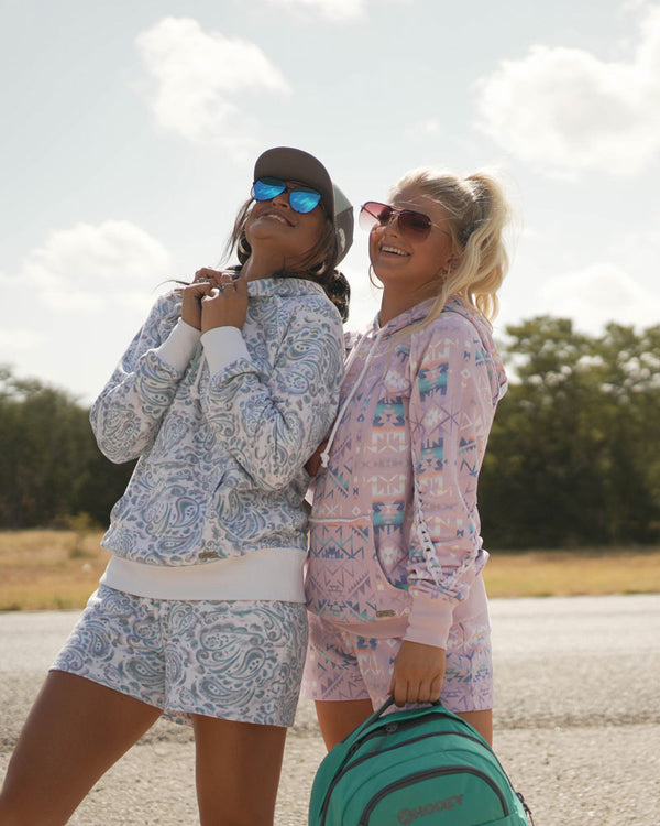 two female models posing together in blue and pink Hooey sets in outdoor setting with turquoise Hooey backpack