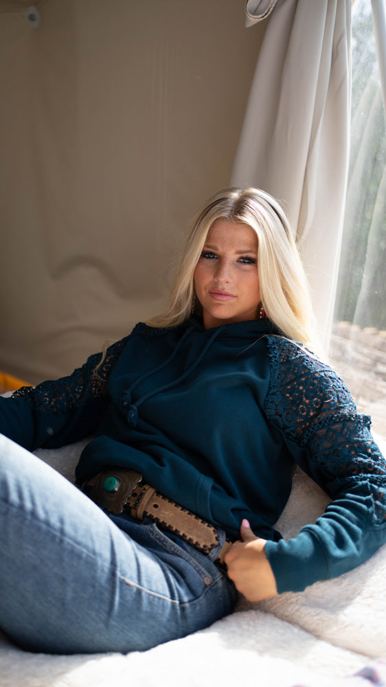 blonde female model wearing medium washed jeans, tan and turquoise Hooey belt, and navy blue hooey hoody