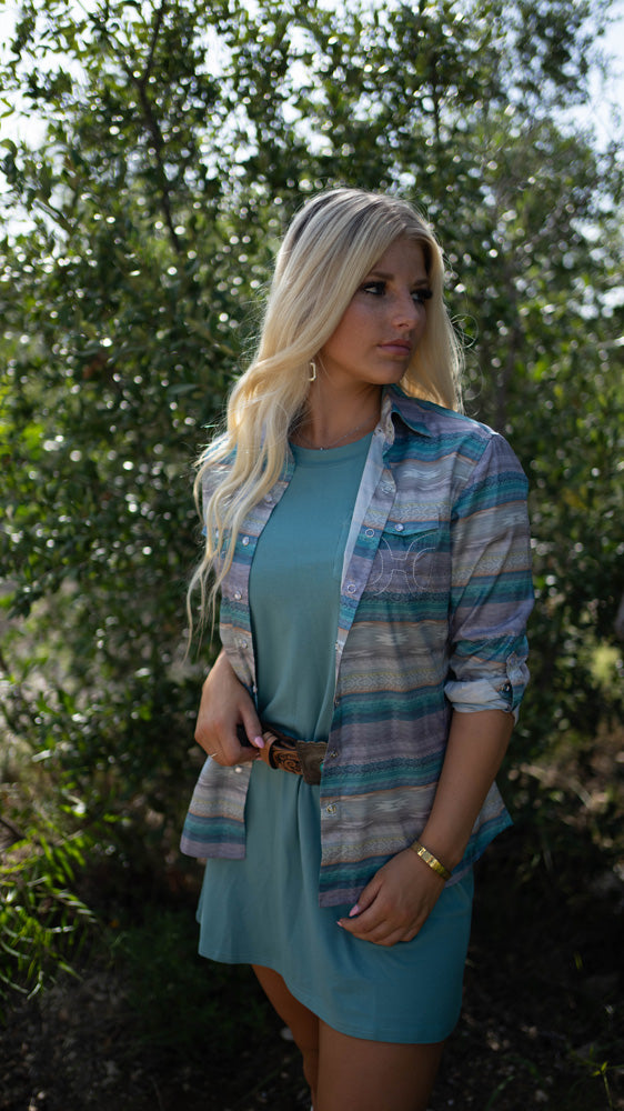 close up of female model posing in blue bamboo dress, brown leather belt, and serape shacket