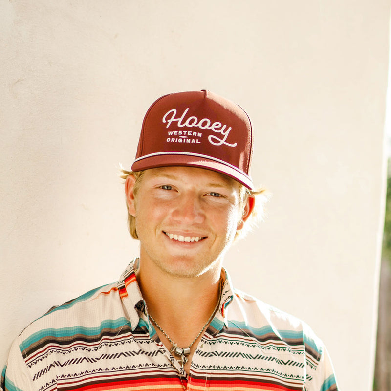 male model posing in red, blue, white pattern golf polo and hooey original hat