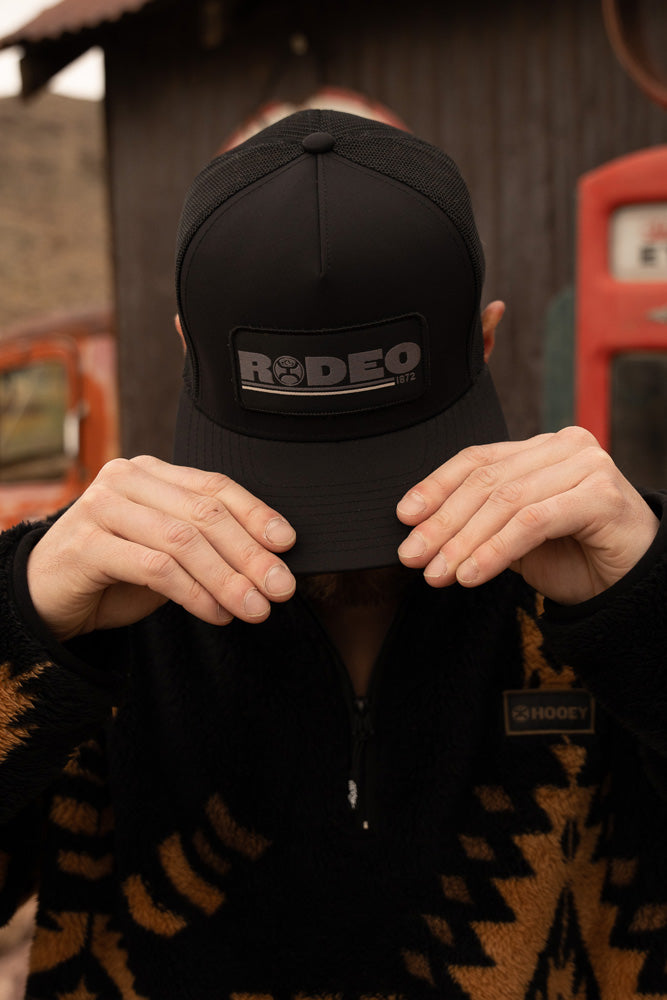 male model holding black on black hooey hat over face wearing black and tan Aztec fleece pullover