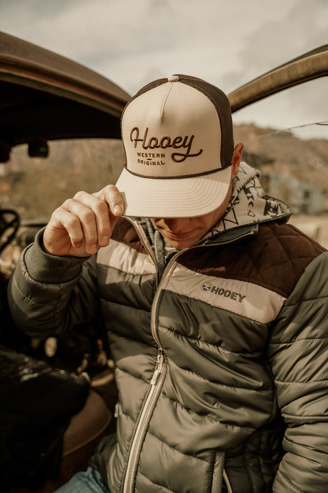 male model wearing olive, cream, brown puffer jacket with tan and brown hooey hat