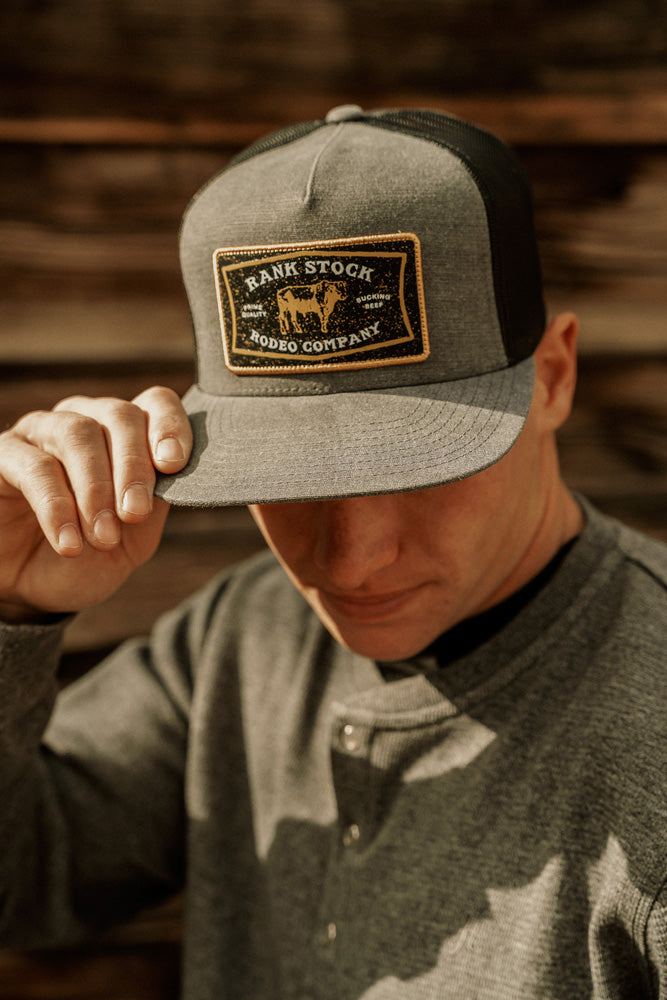 male model sporting grey henley with grey and black rank stock rodeo company hat