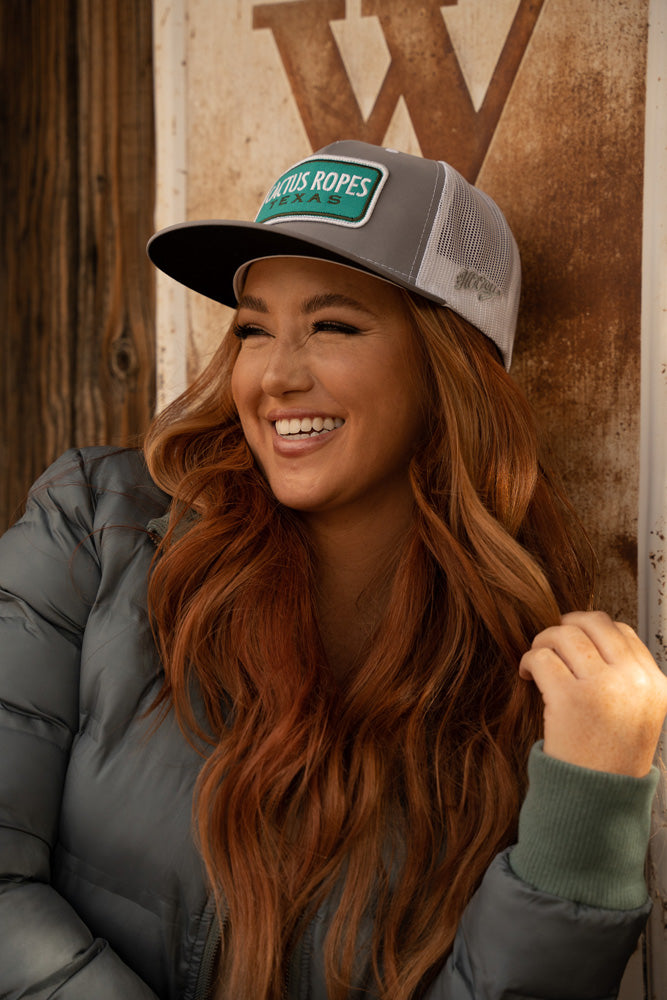 female model wearing grey and white Cactus Ropes hat, and olive puffer jacket 