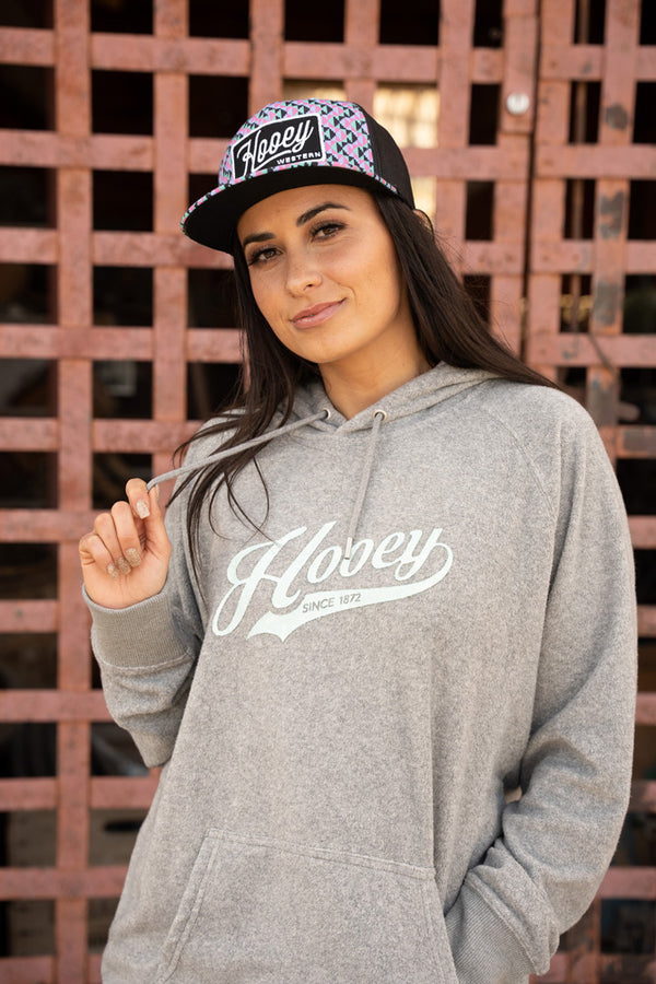 female model wearing the Tulane heather grey hoody with light blue logo, pink, blue, black pattern hat  