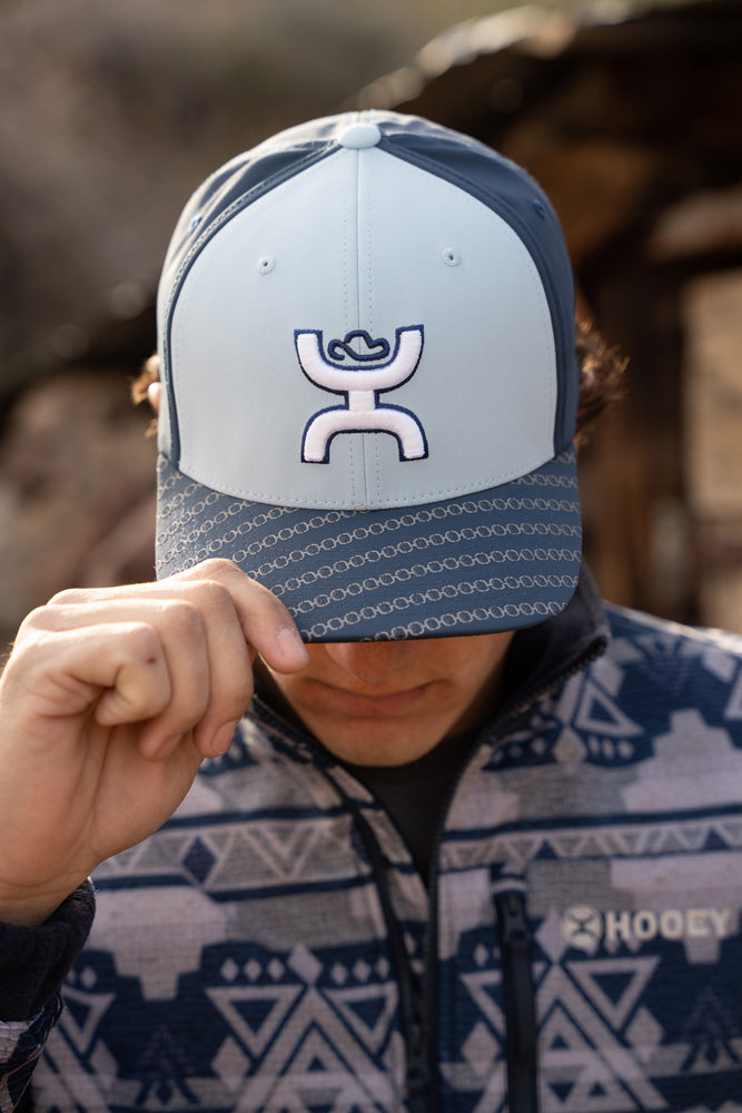 male model posing in navy, fleece, aztec pattern pullover and blue toned hooey hat