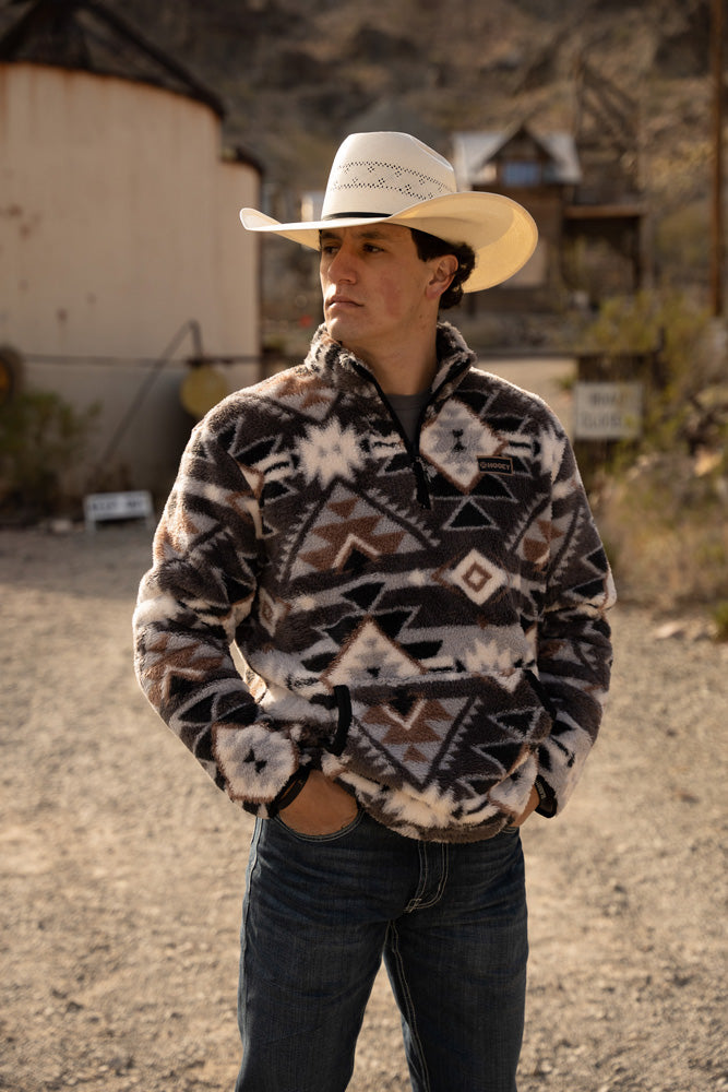 male wearing dark wash jeans, grey fleece pullover and straw cowboy hat