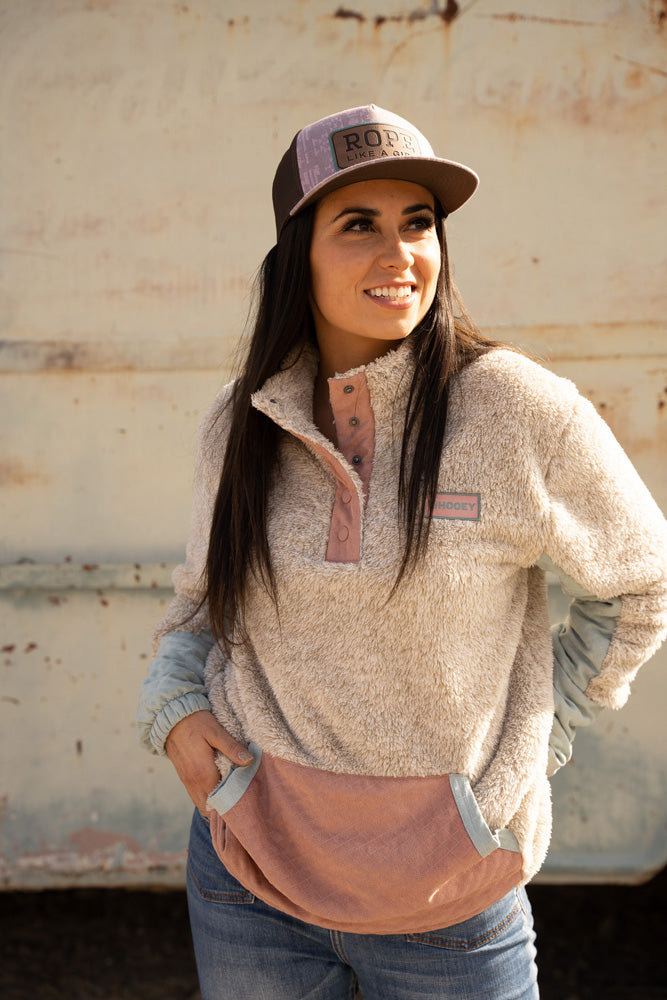 brunette female model wearing blue jeans, pink toned fleece pullover and pink and brown RLAG cap