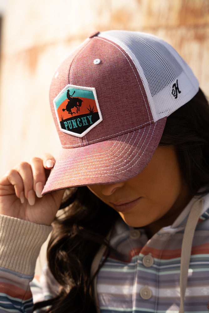 female model wearing purple, rust, blue serape hoody with coral and white punch hat