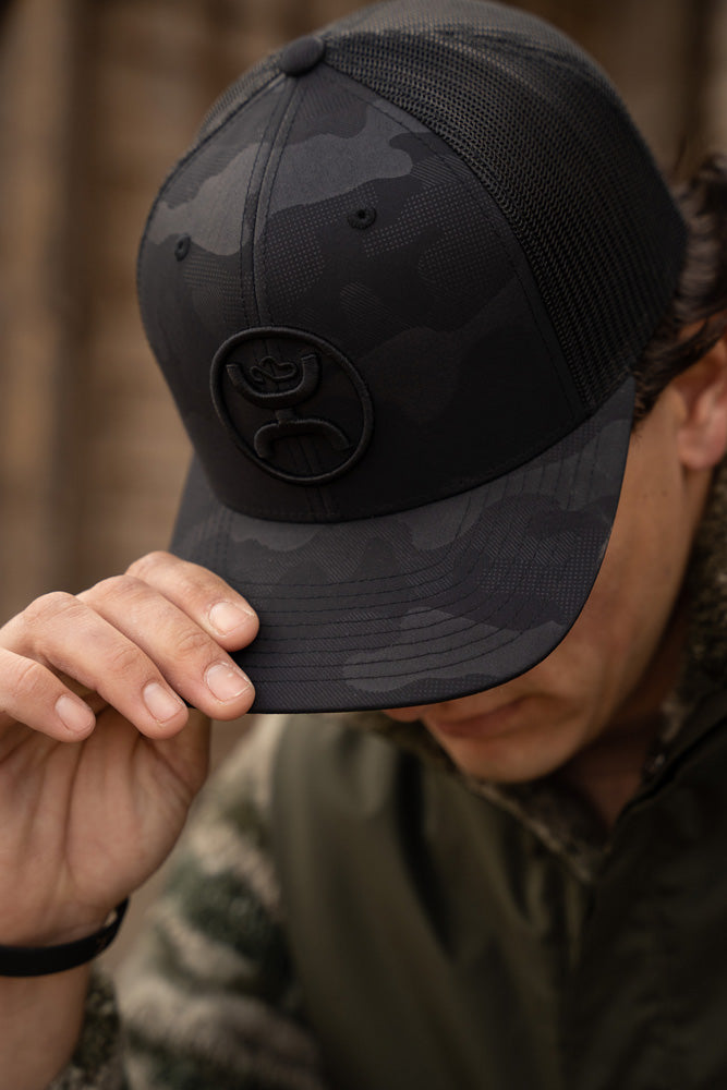 Real model posing with black and gray camo hat pulled over eyes with green fleece and tech jacket