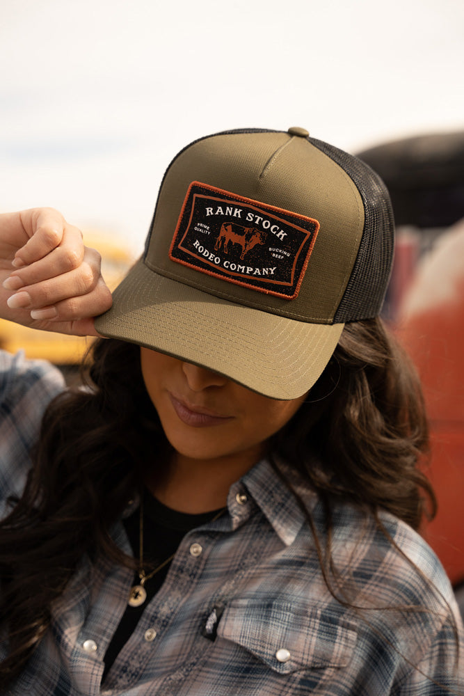 female model wearing blue tone plaid button down with olive and black ranks tock rodeo company hat pulled over eyes