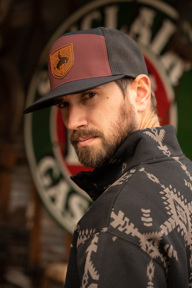 male model posing in black and tan tech jacket and maroon and black hat