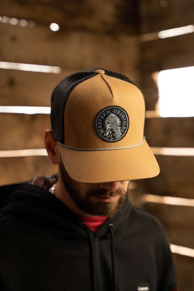 male model sporting black hoody with tan and black hat posing in rustic wooden building