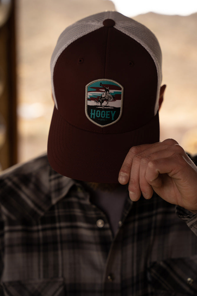 male model wearing burgundy and white Cheyenne hooey hat pulled over eyes with left hand