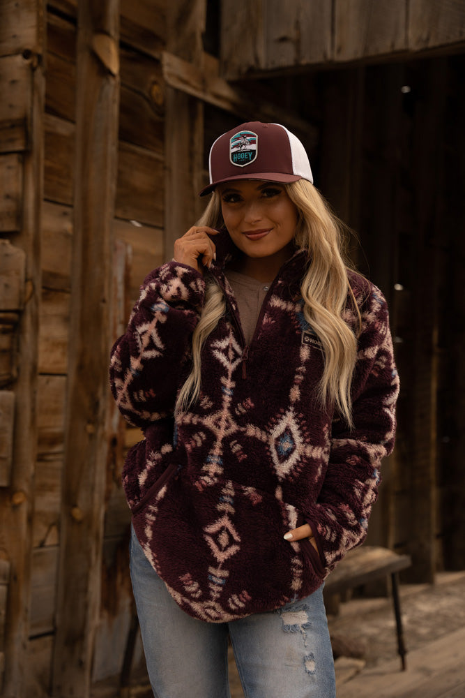 blonde female model posing in light wash jeans, burgundy fleece pullover and burgundy/white hat