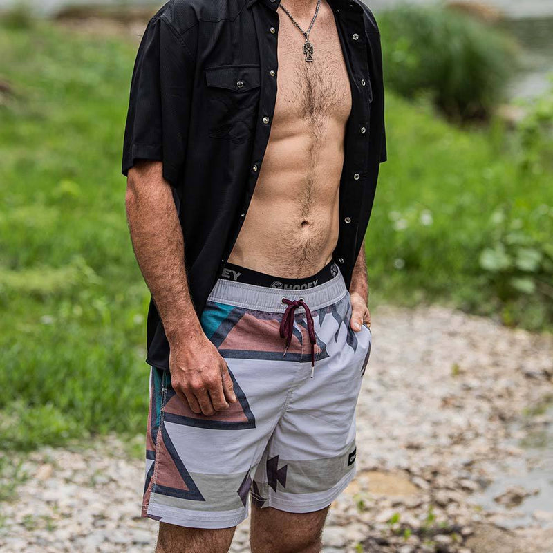 front view of a male model wearing Bigwake cream, brown, turquoise aztec pattern and black SOL shirt on river bank