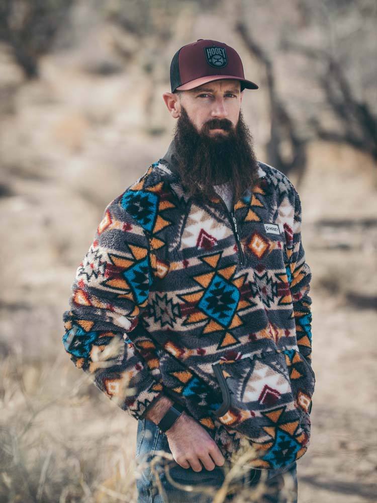 male model wearing the Hooey Fleece Pullover brown, red, yellow, turquoise Aztec pattern in outdoor setting