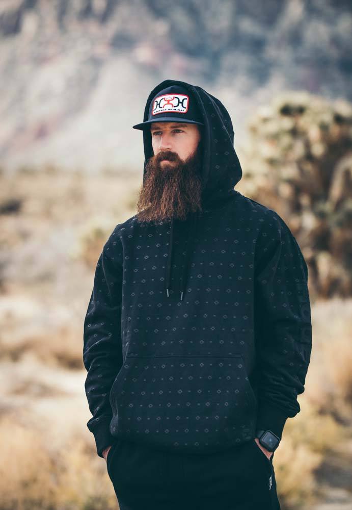 male model wearing the Mesa black hoody with micro grey aztec pattern, black hooey hat, black pants in outdoor setting