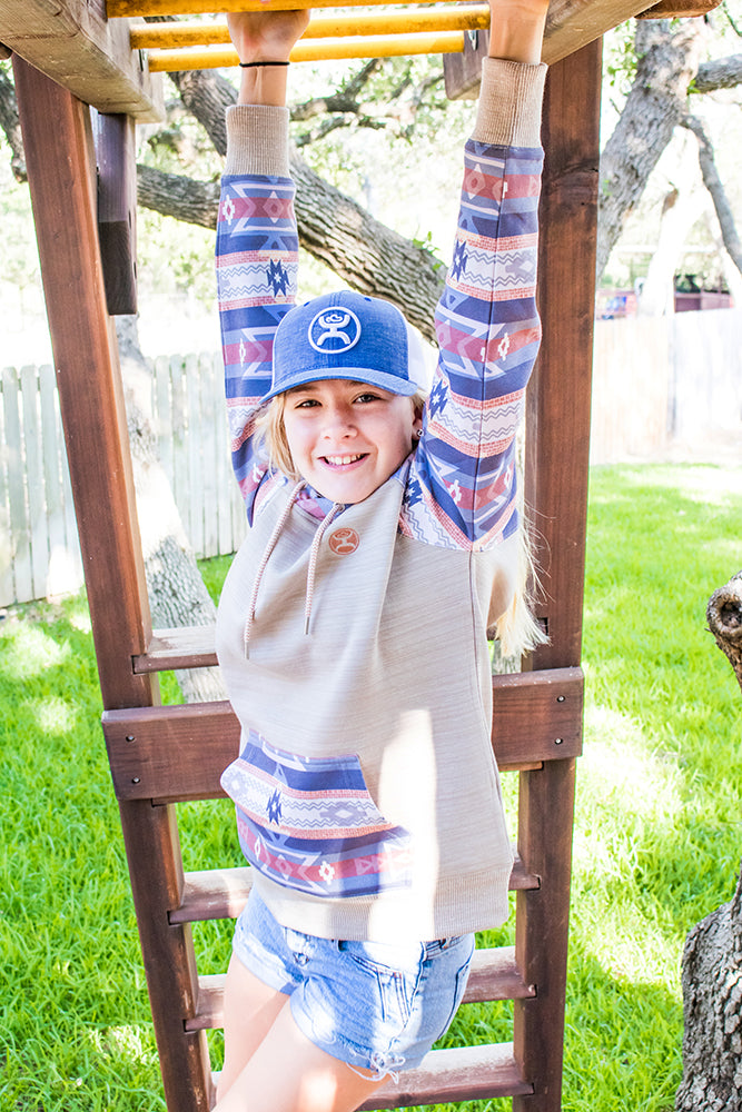 Lifestyle photo of a model sporting the Youth summit cream hoody with pink and blue serape and Aztec pattern on sleeves and pocket